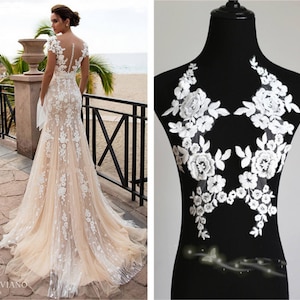 May include: White lace applique with floral designs. The applique is on a black background. The lace is delicate and intricate.