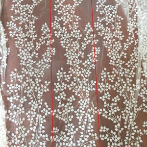 May include: White embroidered floral lace fabric on a sheer mesh background. The design features repeating patterns of delicate white leaves and branches, creating an elegant and intricate look. The lace is shown in a rectangular section, highlighting the detail and texture of the embroidery. This high-quality fabric is perfect for wedding dresses, bridal gowns, veils, and other special occasion garments.