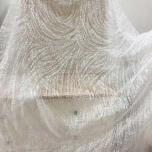 Peut inclure: Tissu de dentelle blanche perl&eacute;e avec un motif en spirale. Le tissu est transparent et d&eacute;licat, avec un l&eacute;ger chatoiement.