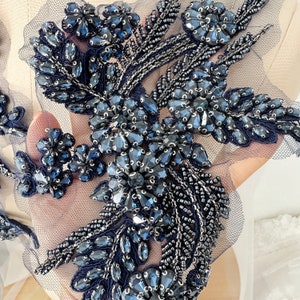 Puede incluir: Una aplicación de flores de cuentas y lentejuelas azul marino. La aplicación está sobre una tela de malla transparente.