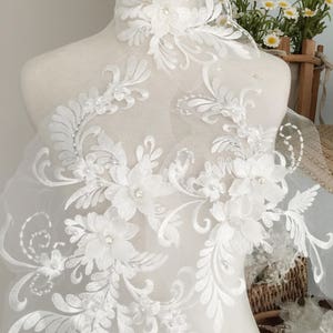 Puede incluir: Borde de encaje blanco floral con adornos de perlas. El encaje es delicado e intrincado, con un patrón floral y cuentas de perlas. Este borde es perfecto para agregar un toque de elegancia a cualquier proyecto.