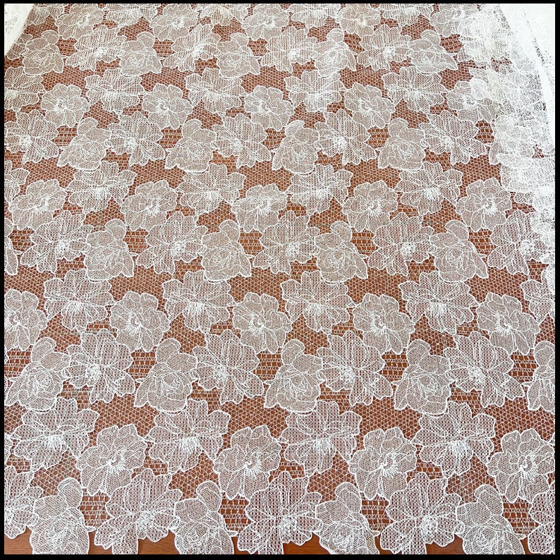 May include: White floral lace fabric with a delicate pattern. The lace has a fine mesh background with intricate floral designs.