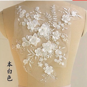 May include: White floral lace applique with delicate beading and intricate details. This lace applique is perfect for adding a touch of elegance to any project.