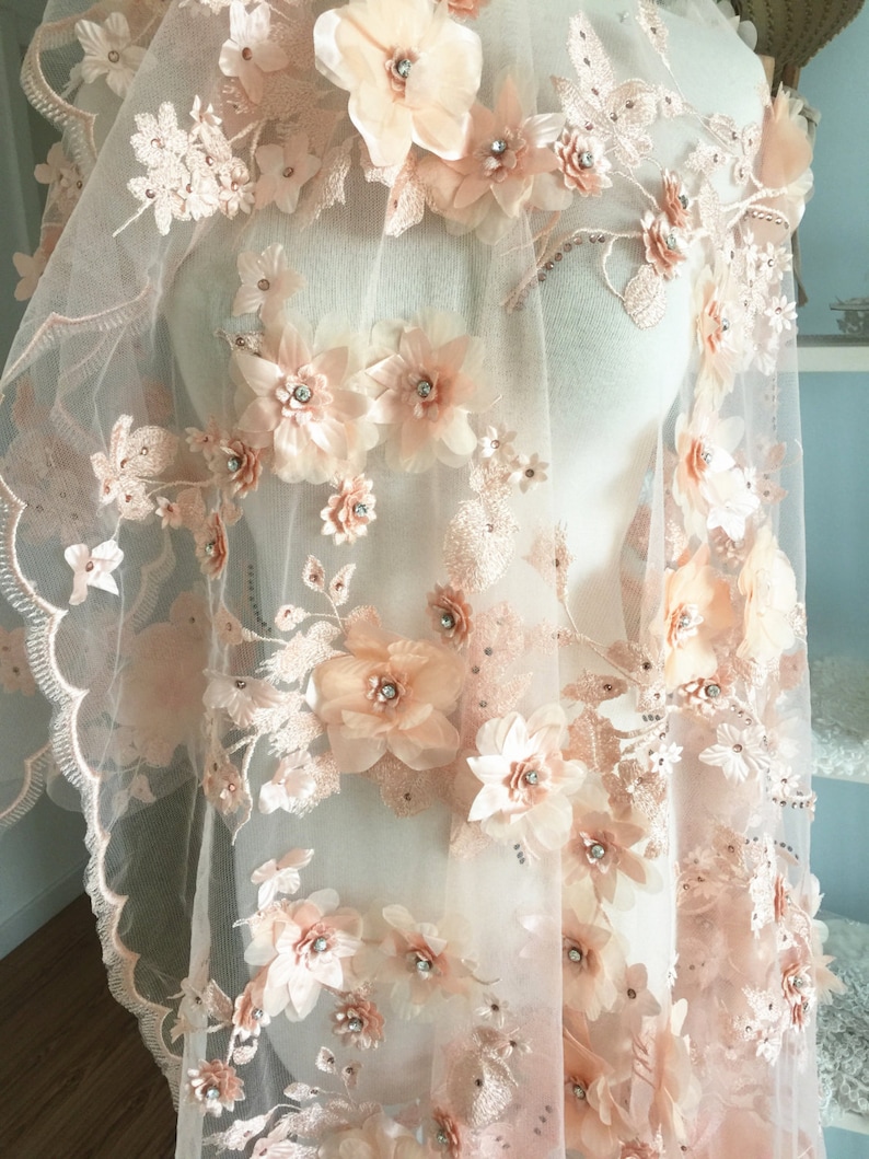 Puede incluir: Tela de encaje floral de color melocot&oacute;n con flores 3D y pedrer&iacute;a. La tela es transparente y delicada, con un borde festoneado.