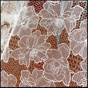 May include: White lace fabric with a floral pattern. The lace is delicate and intricate, with a variety of different flower shapes. The fabric is translucent and has a soft, flowing texture.
