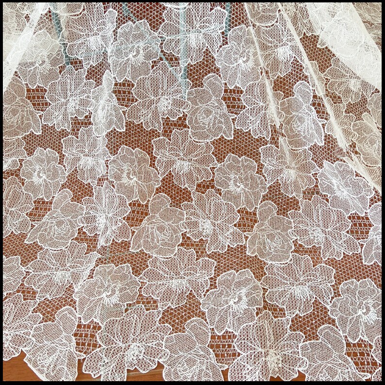 May include: White floral lace fabric with a delicate pattern. The lace is sheer and has a soft, flowing texture.