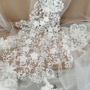 Può includere: Tessuto di pizzo bianco perlato con motivo floreale. Il pizzo è delicato e intricato, con piccole perline sparse ovunque. Il tessuto è perfetto per aggiungere un tocco di eleganza a qualsiasi progetto.