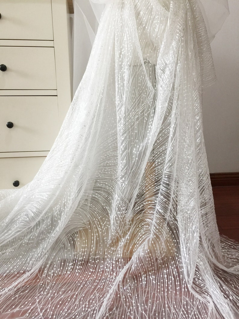 Peut inclure: Tulle blanc avec un motif d&eacute;licat de petits points et lignes blancs. Le tissu est transparent et a une texture douce et fluide.