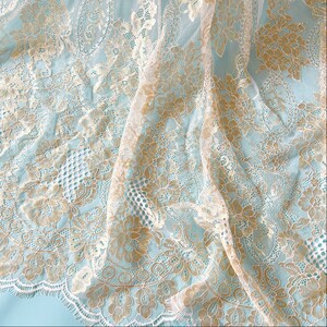 May include: White and gold lace fabric with a delicate floral pattern. The lace is sheer and has a soft, flowing texture.