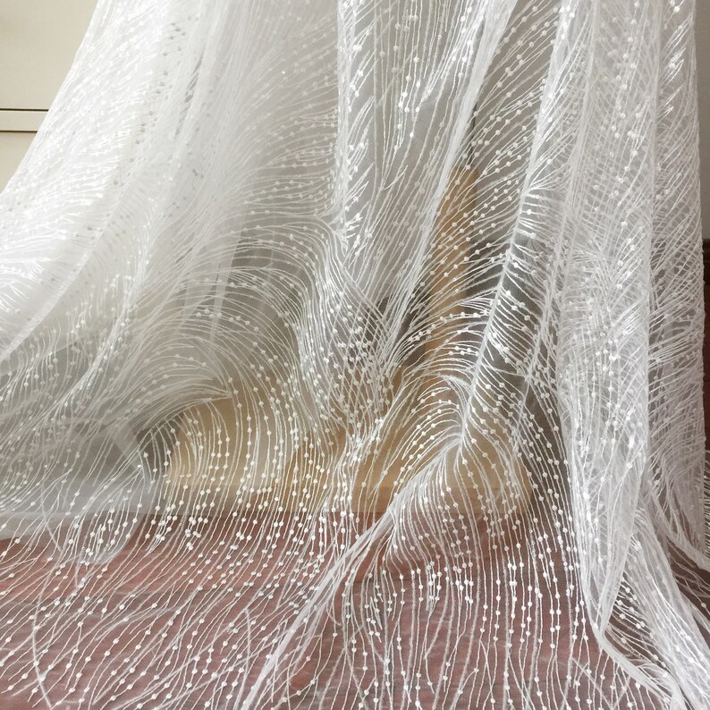 Peut inclure: Tulle blanc avec un motif d&eacute;licat de petits points blancs et de lignes ondul&eacute;es. Le tissu est transparent et a une texture douce et fluide.