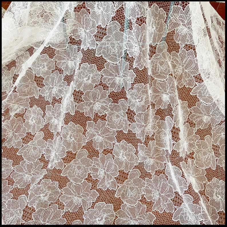 May include: White lace fabric with a floral pattern. The lace is delicate and intricate, with a fine mesh background.