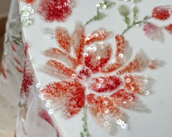 May include: White fabric with a floral pattern made of sequins. The flowers are pink, orange, and green.