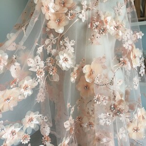 Puede incluir: Tela de encaje floral de color melocot&oacute;n con flores 3D y pedrer&iacute;a. La tela es transparente y delicada, con un tacto suave y rom&aacute;ntico.