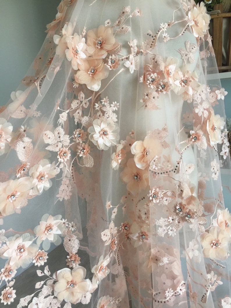 Puede incluir: Tela de encaje floral de color melocot&oacute;n con flores 3D y pedrer&iacute;a. La tela es transparente y delicada, con un tacto suave y rom&aacute;ntico.