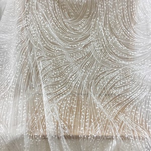 Peut inclure: Tissu de dentelle blanche perl&eacute;e avec un motif en spirale. Le tissu est transparent et d&eacute;licat, avec de petites perles blanches &eacute;parpill&eacute;es.