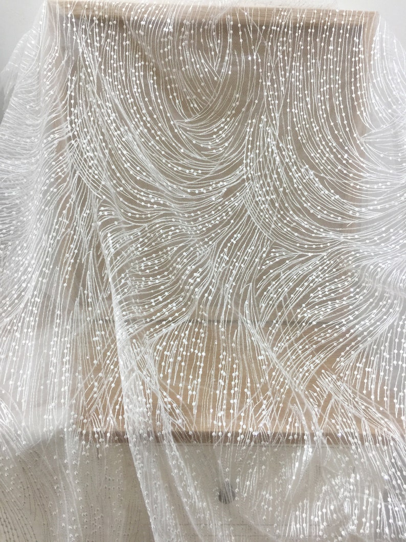 Peut inclure: Tissu de dentelle blanche perl&eacute;e avec un motif en spirale. Le tissu est transparent et d&eacute;licat, avec de petites perles blanches &eacute;parpill&eacute;es.