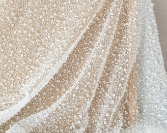 May include: White beaded lace fabric with a delicate, sheer texture. The fabric is covered in small, white beads that create a sparkling effect.