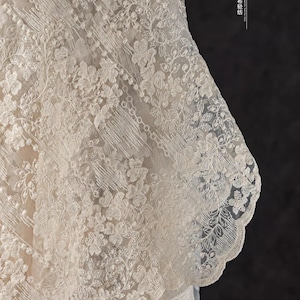 Peut inclure: Gros plan sur une dentelle d&eacute;licate de couleur blanc cass&eacute; avec un motif floral. La dentelle a un bord festonn&eacute; et une texture l&eacute;g&egrave;re et a&eacute;r&eacute;e.