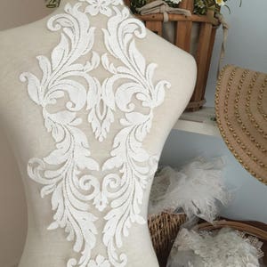 Puede incluir: Aplique de encaje blanco con un dise&ntilde;o floral. El aplique est&aacute; en un maniqu&iacute; blanco y es perfecto para agregar un toque de elegancia a cualquier prenda.