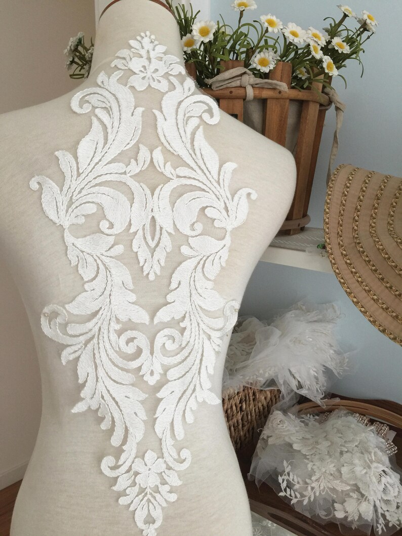 Puede incluir: Aplique de encaje blanco con un dise&ntilde;o floral. El aplique est&aacute; en un maniqu&iacute; blanco y es perfecto para agregar un toque de elegancia a cualquier prenda.
