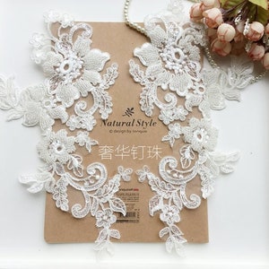 May include: White lace trim with pearl accents. The lace features a floral design with delicate details. The trim is perfect for adding a touch of elegance to any project.