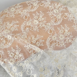 May include: White lace fabric with a delicate floral pattern. The lace has a subtle shimmer and is perfect for adding a touch of elegance to any project.