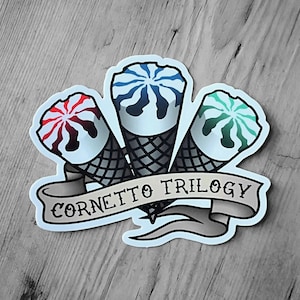 May include: A sticker depicting three ice cream cones with red, blue, and green swirls on waffle cones. The sticker includes a banner that reads "CORNETTO TRILOGY" in a tattoo style, set against a wooden background.