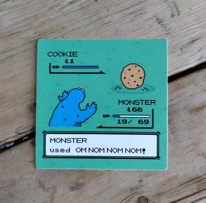 K&ouml;nnte beinhalten: Ein quadratischer, gr&uuml;ner Untersetzer mit einem pixeligen Cookie Monster und einem Schokoladen-Chip-Cookie-Design. Das Design imitiert eine Retro-Videospiel-Oberfl&auml;che mit den Texten "COOKIE", "MONSTER" und "OM NOM NOM NOM!"