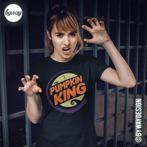 Puede incluir: Una camiseta negra con un dise&ntilde;o gr&aacute;fico morado, naranja y amarillo que dice "The Pumpkin King".