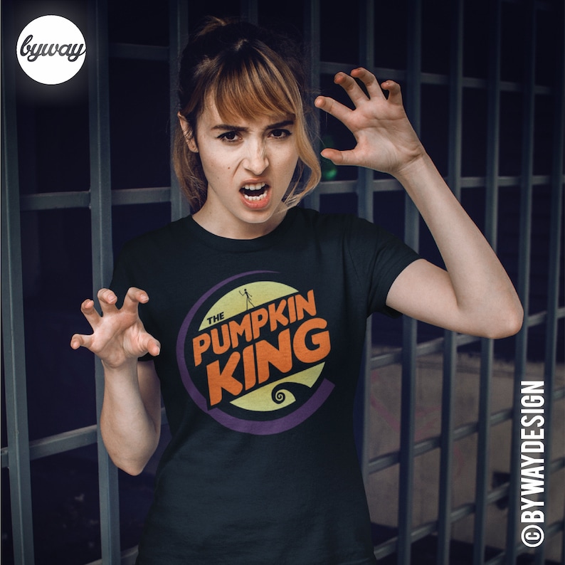 Puede incluir: Una camiseta negra con un dise&ntilde;o gr&aacute;fico morado, naranja y amarillo que dice "The Pumpkin King".