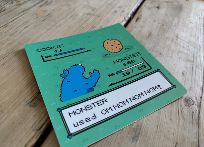 K&ouml;nnte beinhalten: Eine gr&uuml;ne Karte mit einem pixeligen Cookie Monster und einem Keks. Die Karte enth&auml;lt Text mit der Aufschrift "COOKIE" und "MONSTER" mit Gesundheitsbalken und dem Satz "MONSTER used OM NOM NOM!"