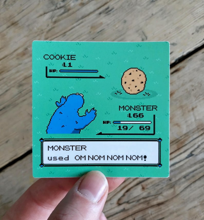 K&ouml;nnte beinhalten: Ein quadratischer Aufkleber mit einem pixeligen Cookie Monster-Charakter und einem Schokoladen-Chip-Keks auf gr&uuml;nem Hintergrund. Der Text lautet "COOKIE: L1" und "MONSTER: L66". Der Text unten lautet "MONSTER used OM NOM NOM NOM!"
