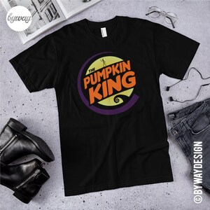 Puede incluir: Camiseta negra con un gr&aacute;fico de un c&iacute;rculo morado con el texto "The Pumpkin King" en letras naranja y amarillas. El gr&aacute;fico tambi&eacute;n incluye una silueta de Jack Skellington de la pel&iacute;cula "Pesadilla antes de Navidad".