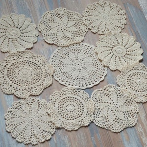 Può includere: Dieci tovagliette all'uncinetto color crema, con diversi motivi, disposte su una superficie in legno chiaro.