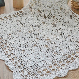 May include: White crocheted table runner with a delicate floral pattern. The runner is made of cotton and has a scalloped edge.