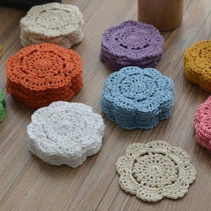 Può includere: Un set di dieci sottobicchieri all'uncinetto in vari colori, tra cui bianco, beige, azzurro, rosa, verde e arancione. I sottobicchieri sono tutti circolari e hanno un design delicato e traforato.