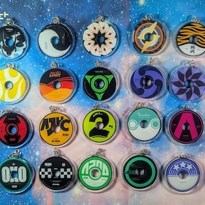 May include: A collection of clear acrylic keychains with various colorful designs. Each keychain is circular with a hole in the center, resembling a CD. Designs include geometric patterns, abstract shapes, and text. The keychains are displayed against a blue background.