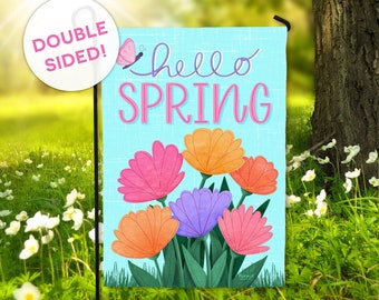 May include: A double-sided garden flag with a blue background and the text "hello spring" in pink lettering. The flag features a colorful bouquet of flowers and a pink butterfly.