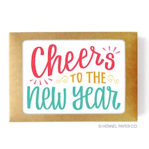 May include: A brown card with a white background and the text "Cheers to the new year" in colorful lettering. The card is in a brown envelope.