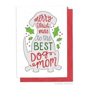 May include: A white Christmas card with a gray dog silhouette. The card says "merry christmas to the best dog mom". The dog is surrounded by green holly leaves and red berries.