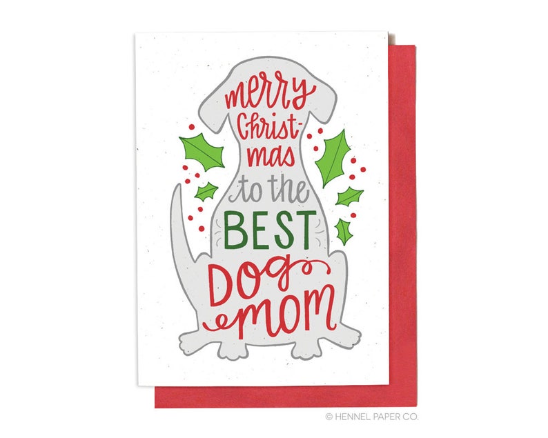 May include: A white Christmas card with a gray dog silhouette. The card says "merry christmas to the best dog mom". The dog is surrounded by green holly leaves and red berries.