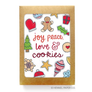 May include: A white card with a brown border and a festive Christmas design. The card features a variety of colorful illustrations of Christmas cookies, ornaments, and other holiday symbols. The text "joy, peace, love & cookies" is written in red and orange lettering.