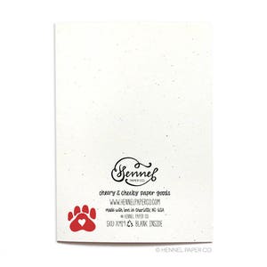 May include: A blank greeting card with a red paw print and a heart. The back of the card has the text "Sennel Paper Co. Cheery & Cheeky Paper Goods. www.hennelpaperco.com Made with love in Charlotte, NC-USA Sennel Paper Co. SKU:XM19 Blank Inside &copy; Hennel Paper Co."