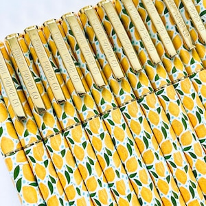 May include: A collection of pens with a vibrant lemon pattern. The pens have gold-colored clips with the text "Hennel Paper Co" embossed on them. The design features yellow lemons, green leaves, and small blue dots on a white background.