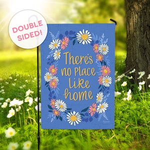 May include: A blue garden flag with a wreath of white and pink daisies. The text "There's no place like home" is written in a gold script font.