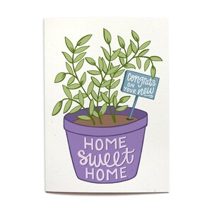 May include: A purple potted plant with green leaves and a blue sign that says "Congrats on your new home" in white lettering. The pot has the words "Home Sweet Home" written on it in purple.
