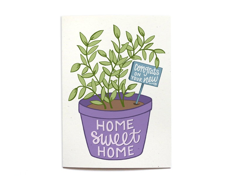 May include: A purple potted plant with green leaves and a blue sign that says "Congrats on your new home" in white lettering. The pot has the words "Home Sweet Home" written on it in purple.