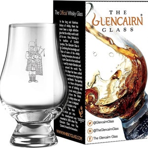 Puede incluir: Un vaso de whisky Glencairn transparente con una imagen grabada de un gaitero. El vaso se muestra junto a su embalaje, que presenta el texto "The Glencairn Glass" y una salpicadura de l&iacute;quido &aacute;mbar.
