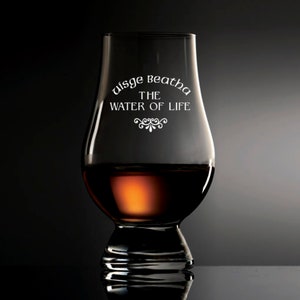 Puede incluir: Una copa de whisky transparente, en forma de tulip&aacute;n, llena de l&iacute;quido &aacute;mbar. La copa tiene el texto blanco "Uisge Beatha THE WATER OF LIFE". La copa est&aacute; sobre una superficie oscura.