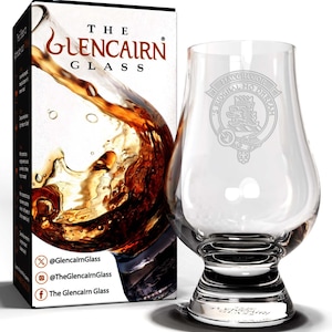 May include: A clear glass Glencairn whisky glass with an etched design of the MacGregor clan crest. The crest features a lion holding a sword and the text "MacGregor Ogha Mo Dhreah". The glass is sitting on a white surface.